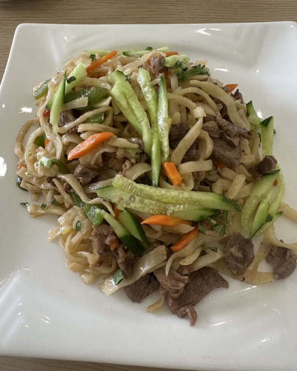 A plate of fried noodles with meat, cucumber and carrot